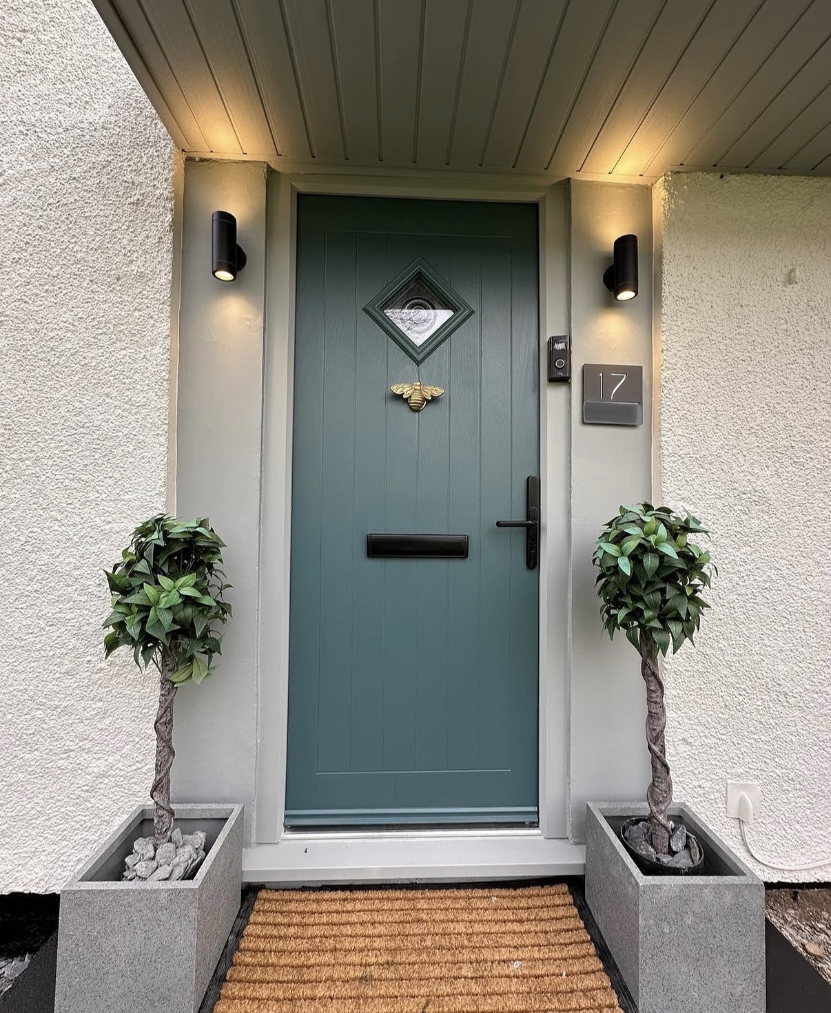 Green door with plants and welcome mat.