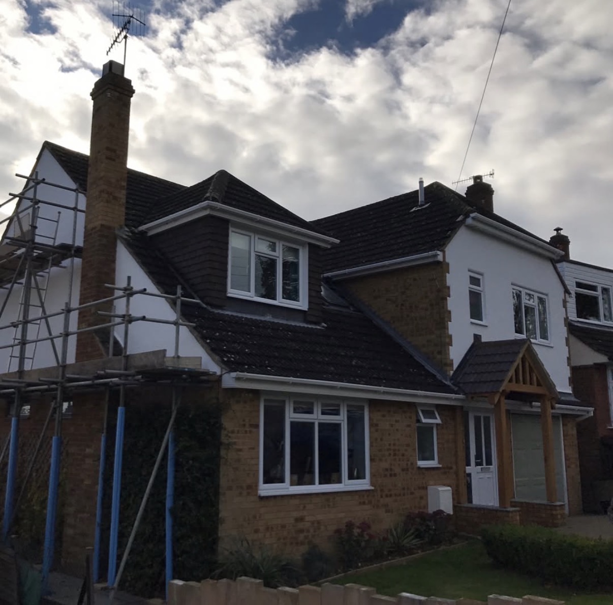 Two-story house with scaffolding and cloudy sky.